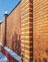 Modern red brick fence with turrets, in winter, outdoors © clairelucia
