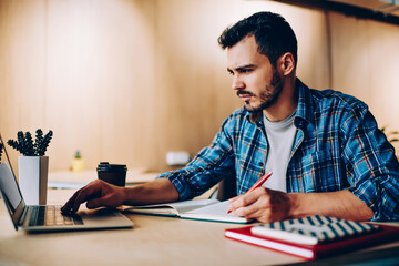 Serious caucasian man searching useful information for university course work sitting with modern...