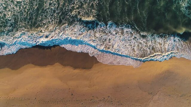 Aerial drone view of beautiful sunrise over the sea. Waves washing beach sand.
