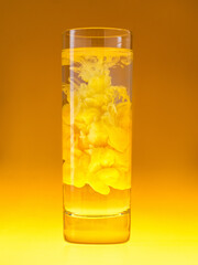 Ink cloud in clean glass. Yellow paint in water. Monochrome scheme. Concept of creative cocktails.