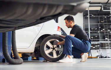 Fototapeta na wymiar Man in work uniform repairs car indoors. Conception of automobile service