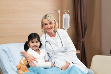 Portarit of smaile doctor pediatrician and little girl patient on bed with teddy bear