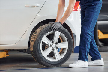 Close up view of man in work uniform with car wheel indoors. Conception of automobile service