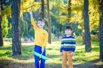 Happy two brother kids playing with toy airplane against blue summer sky background. Boys throw foam plane in the forest or park. Best childhood concept