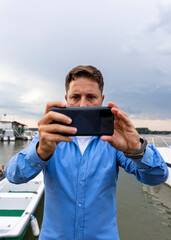 Man holding smartphone in his hands at river and taking photographs