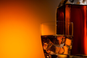 a glass of whiskey on the rocks on a dark orange background, next to a bottle of Bourbon