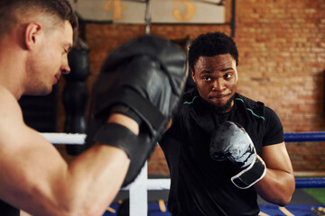 Fototapeta na wymiar Having boxing practive. African american man with white guy have workout day in gym