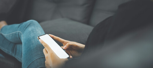 Close-up of hand holding mockup white screen mobile phone on sofa in living room.