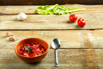 A plate of clay borscht with chicken with a spoon on a wooden table near vegetables.