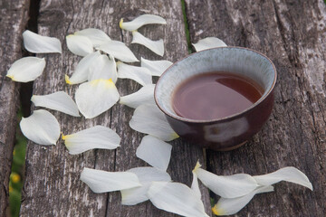 Cup of chinese tea with petals os narcissus on old wooden table