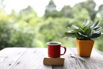 Red coffee mug on top of old book with plant pot on rustic wooden table