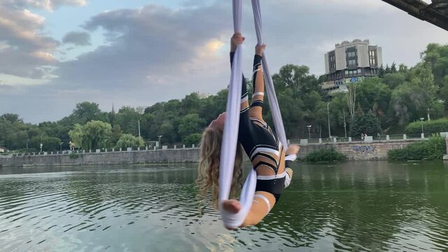 Child girl aerialist performs gymnastic split and spins on hanging aerial silk.