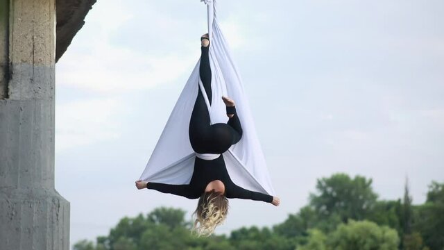 Woman aerialist performs acrobatic tricks on hanging aerial silk and waving by fabric.