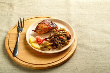 A plate with vegetables and a piece of chicken baked on a round stand on a wooden table with a fork.