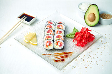 Diet sushi roll with cream cheese, tuna, shrimp and salmon on a white plate in a composition with ingredients