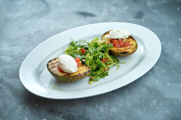 Grilled avocado with tomato salsa and cream cheese and salad in a white plate