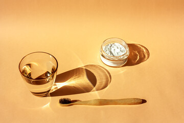 Bamboo toothbrush, glass of water and toothpaste powder on a peach-colored pastel background. Biodegradable pesonal care and plastic free zero waste concept. Top view. Shadows.