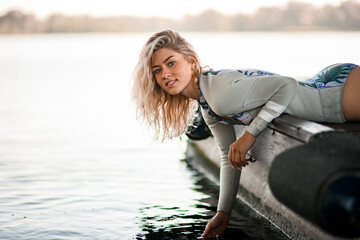 young beautiful blonde woman in swimsuit lies on the pier and picks up water