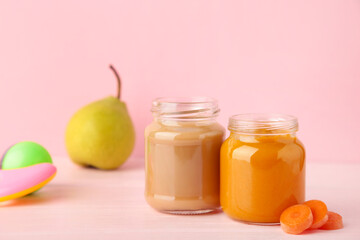 Glass jars with nutrient baby food on pink background