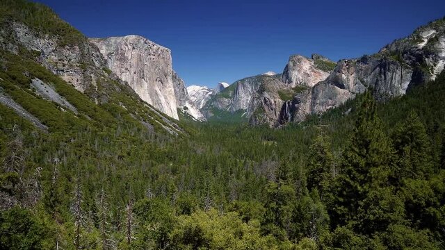 A slow motion tilt up shot of the famous Yosemite valley from a famous picture spot showing all the mountains and waterfalls on a warm summer day in California.