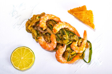 Shrimps with stewed vegetables, lime wedge, croutons and creamy garlic sauce on a white surface.