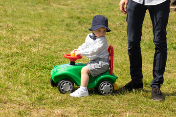 Father and son concept. Child playing on green car with father standing next to him on green meadow during sunny summer day