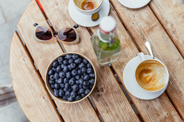 Blueberries in carton container with two empty cup of coffee at wooden table
