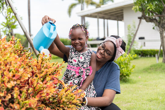 Smile African Girl Help Mother Water The Plants At Outdoor Her Home Garden. - Happy Family Lifestyle Concept.