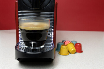A delicious coffee with foam made by a capsule coffee maker and several colored capsules next to it.