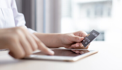 Fototapeta premium Young woman holds a credit card to make purchases online in the tablet.