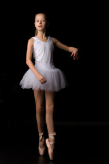 Naklejka premium Cute little girl in a tutu and pointe shoes is dancing in the studio on a black background.