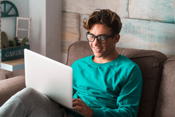 Young caucasian student study at home with internet and laptop computer sitting on the couch - home...