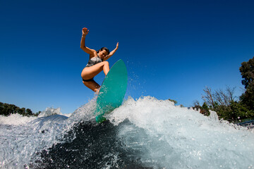 Active sporty woman wakesurfer in gray swimsuit jumps with bright surf board