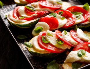 Caprese zucchini stuffed with tomatoes and mozzarella cheese with basil leaves and olive oil prepared for baking in a baking dish close up view