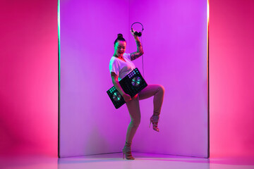 Chill time. Young female musician in headphones performing on purple background in neon light. Concept of music, hobby, festival, entertainment, emotions. Joyful party host, DJ, portrait of artist.