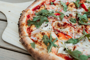 Fresh vegetarian pizza with tomato, mozzarella cheese, mushrooms and arugula, served on a wooden board