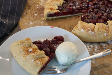 Summer homemade galette with cherries on parchment paper and ice cream. Summer French open pie.  
