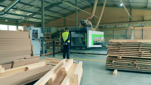 Man in uniform works with factory machine, processing wood.