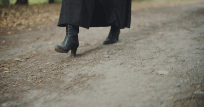 View of woman legs in black shoes walk through the forest, wearing black skirt, gothic style picture. Woman walks fast wearing long dress. Close up on shoes. Summertime green background.
