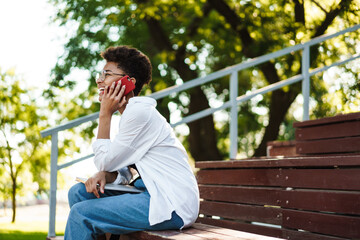 Fototapeta premium Woman sitting outdoors while talking by mobile phone