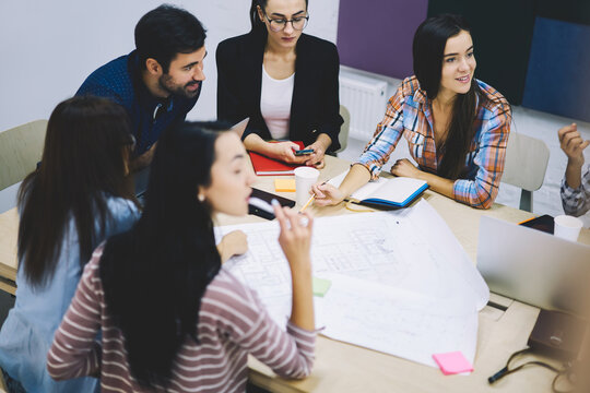 Young crew of male and female graphic designers communicating with each other and discussing ideas for creating new project sitting in office interior with sketch during brainstorming session