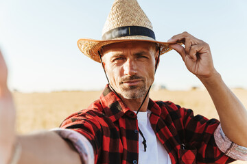 Fototapeta premium Image of adult man taking selfie photo while standing at cereal field