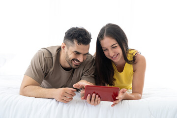 Happy young couple using mobile phone while lying on the white bed in the bedroom at home.