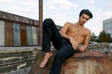 Handsome athlete and sexy young man with naked torso lying on old abandoned roof.
