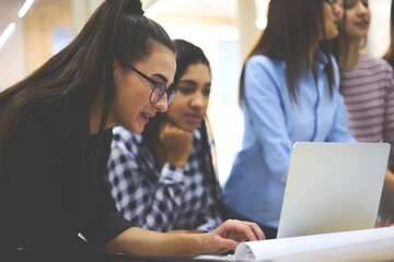 Fototapeta premium Good looking positive hipster girl chatting with friends in social networks using application and texting feedback on website via modern laptop and 4G internet while having work break in office