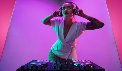 Summertime. Young female musician in headphones performing on purple background in neon light....