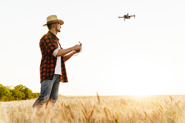 Image of focused handsome man using drone while standing at cereal field