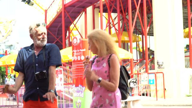 Happy senior couple eating ice cream and dancing together  at the amusement park outdoors in summer.  crazy old man and funny mature woman  having fun in vacation