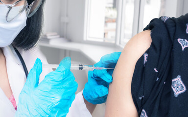 Doctor makes vaccination in the shoulder of female patient in a hospital. Vaccine or flu shot in injection needle.