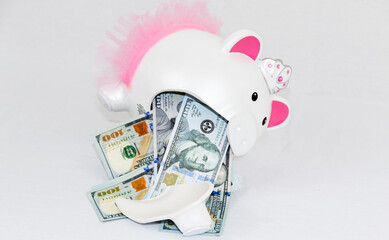 White broken piggy bank with pink ears and tutu with one hundred dollar bills spilling out